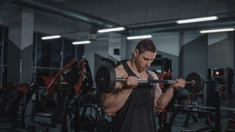 Een man doet biceps curls met een halterstang in een sportschool