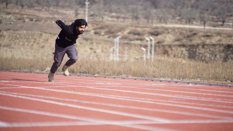 Een man zet een sprint in op een atletiekbaan in een heuvelachtig landschap