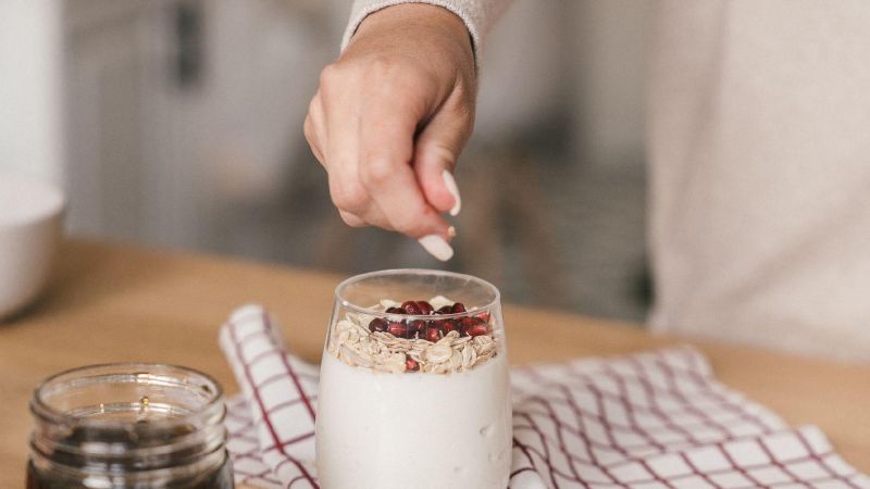 Iemand strooit havermout en granaatappelpitten over een glas yoghurt
