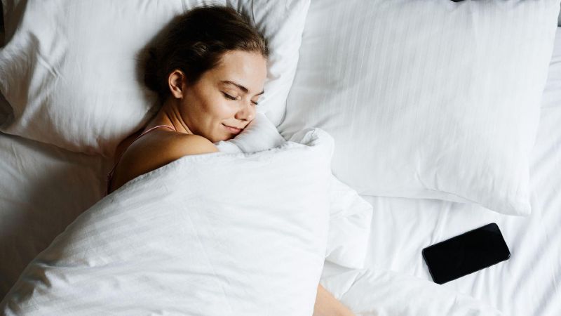 Een vrouw slaapt in bed met haar telefoon naast zich op het laken